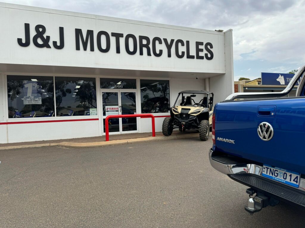 Exterior view of J&J Motorcycles store with motorcycles visible through the window, and a blue Volkswagen Amarok parked in front, featuring an onsite IT support company in attendance.